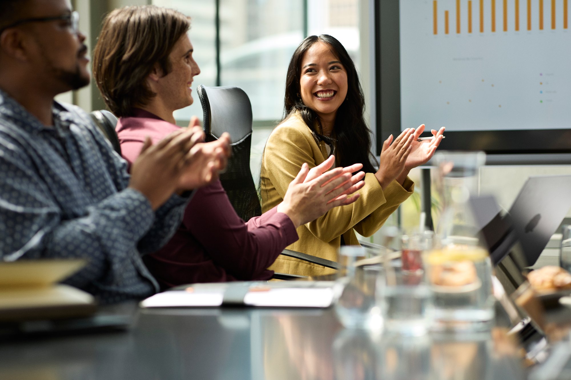 3 office workers smiling and clapping during meeting presentation