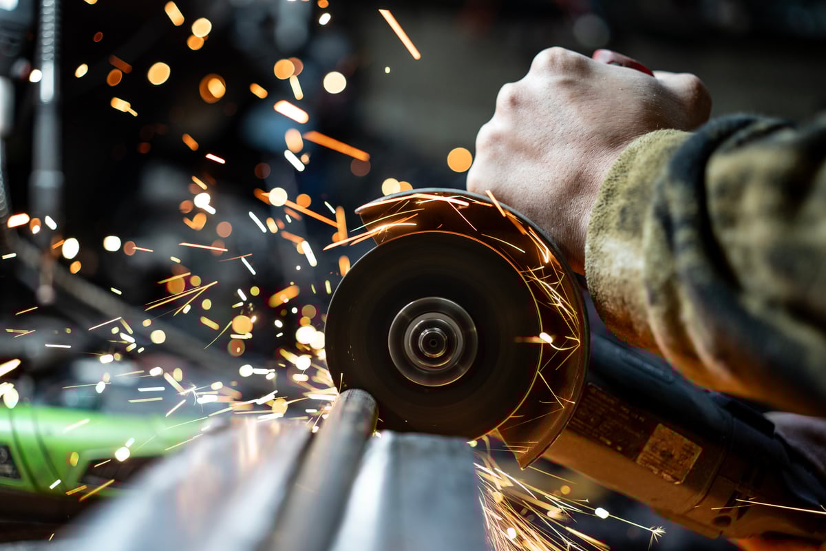 Close up of worker's hand, power sawing through metal pipe