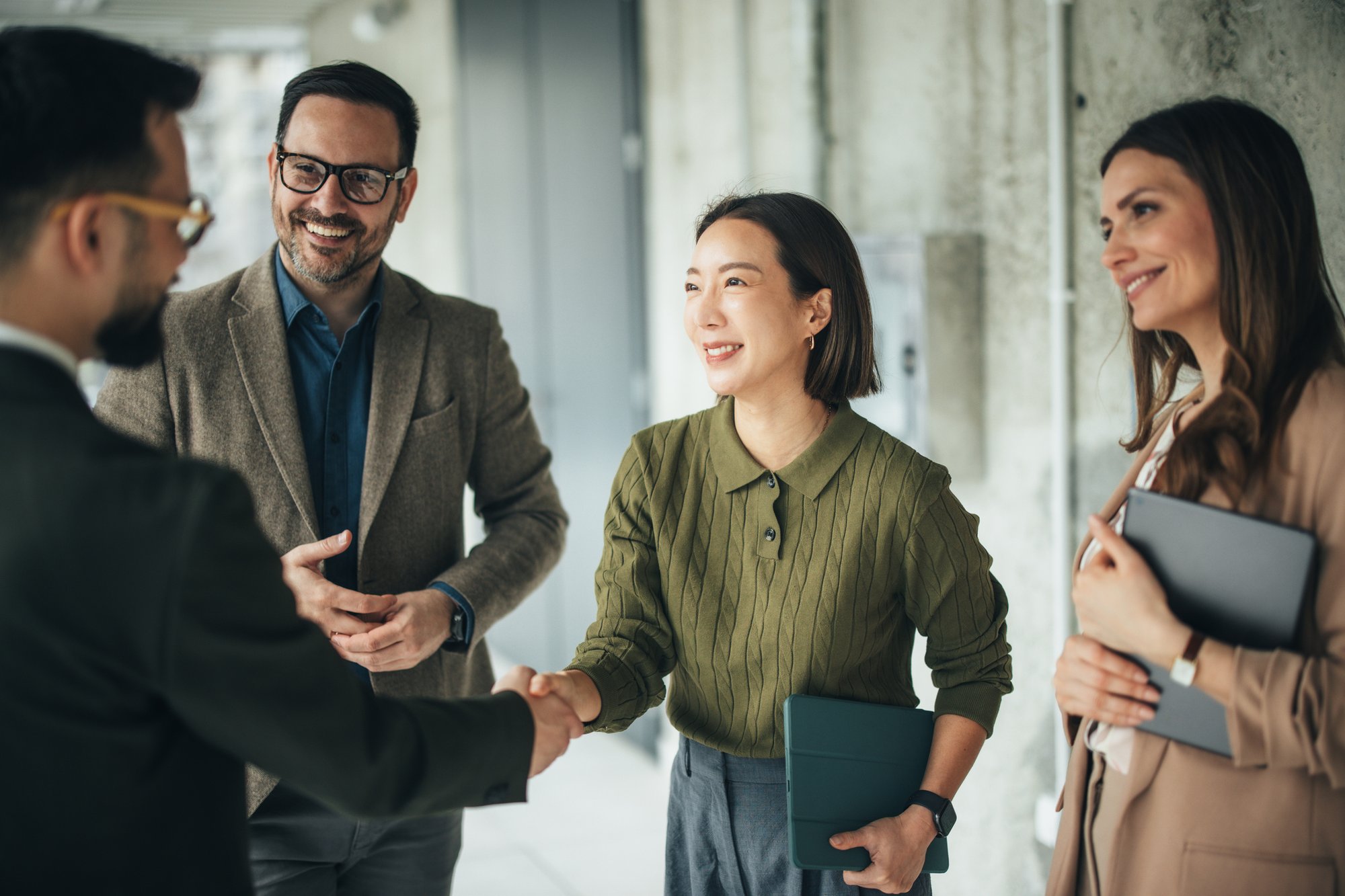 Group of professionals meeting in a hallway, shaking hands, carrying tablets