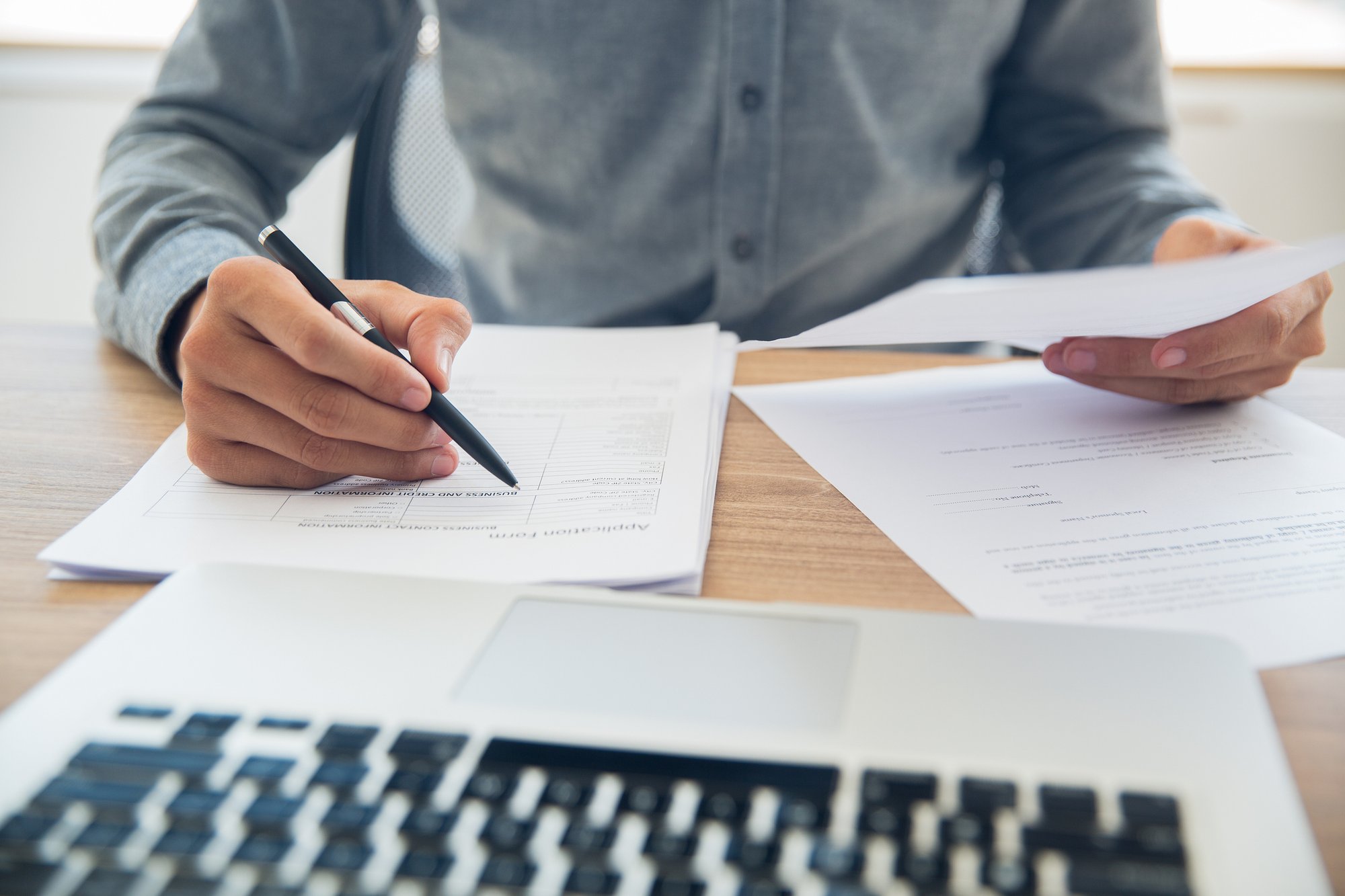 Person filling in printed forms in front of laptop