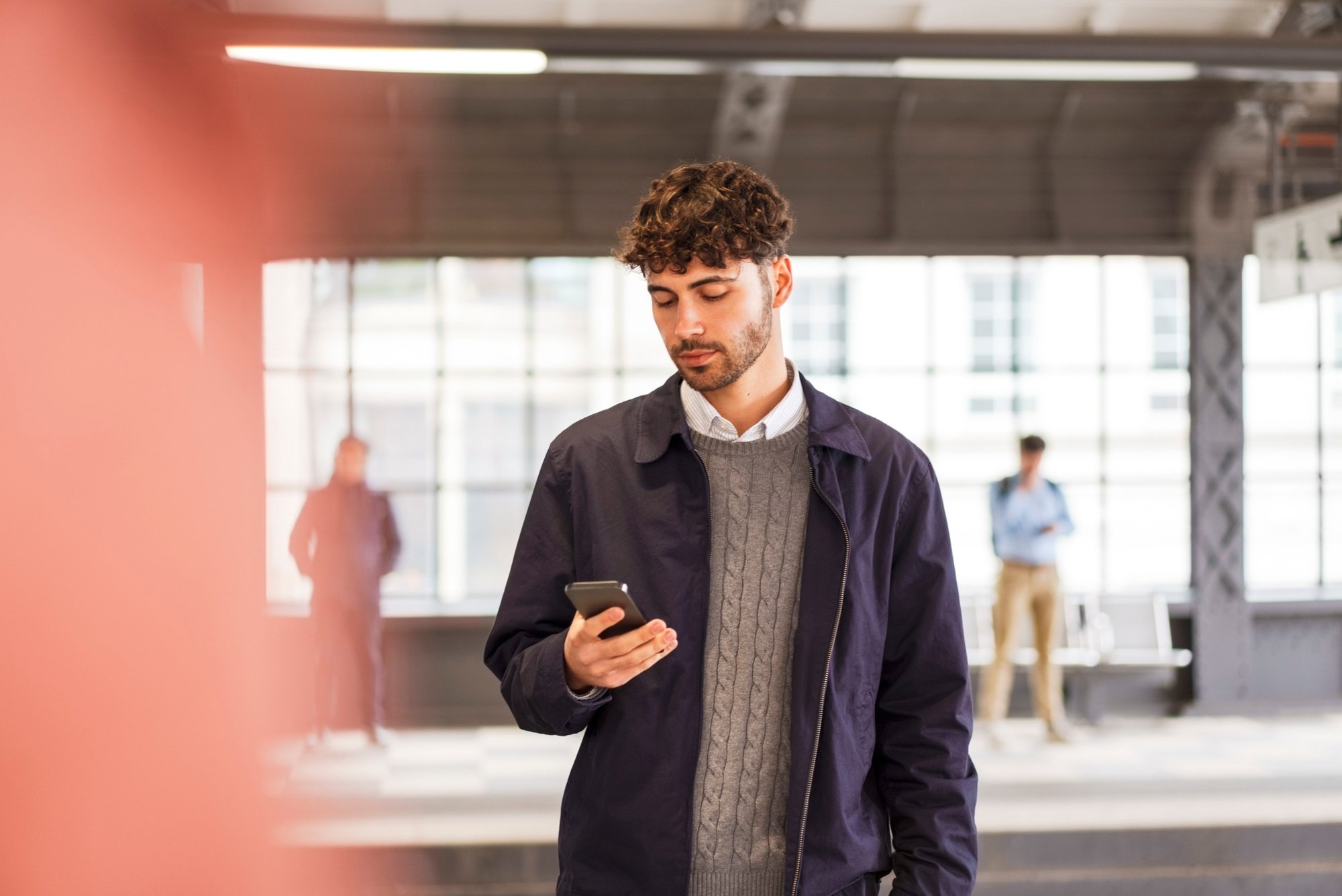 Man looking at phone, walking away from bus stop