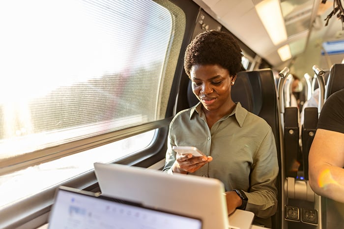 Woman riding train, working on phone and laptop