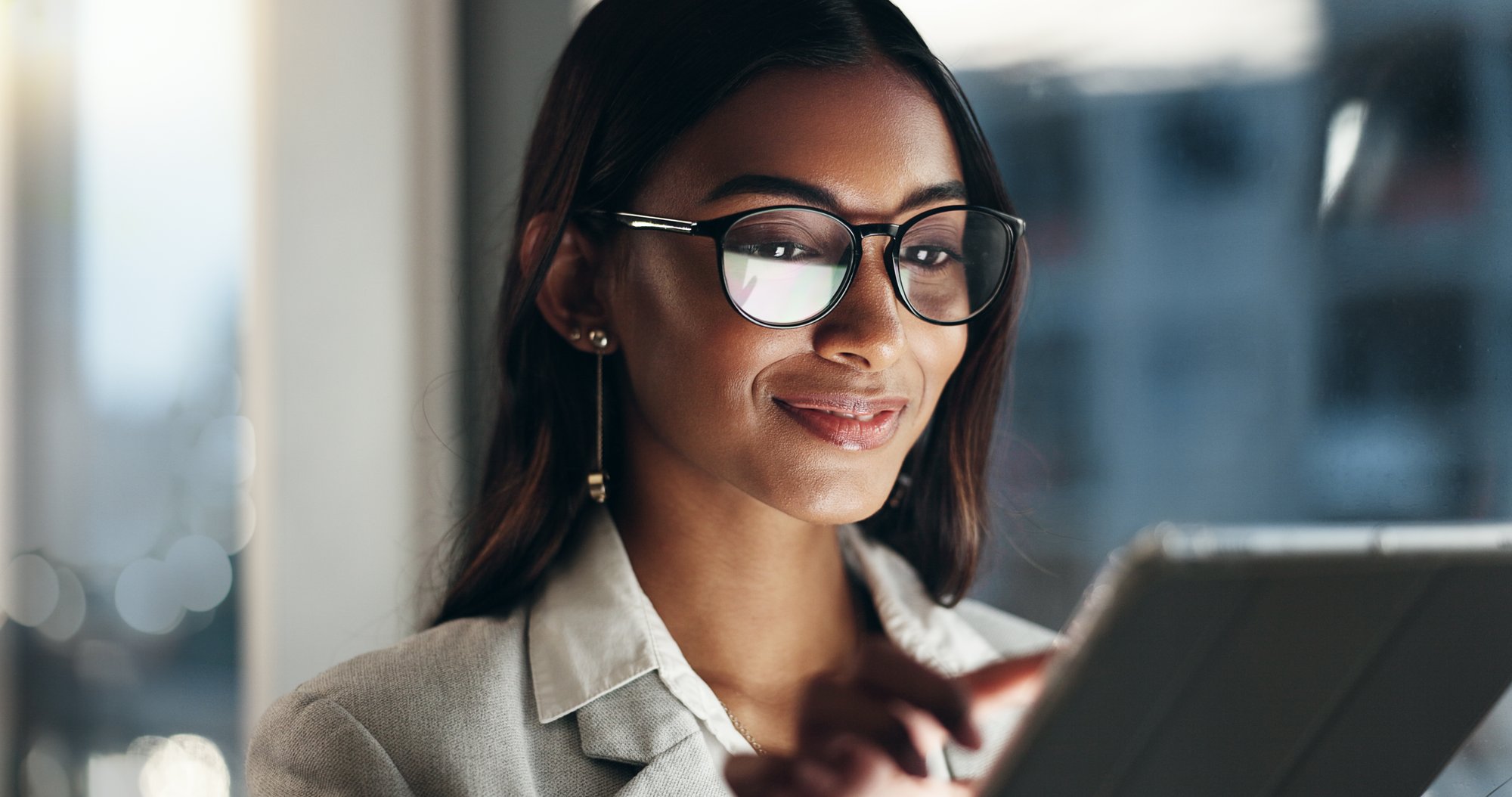 Woman with glasses smiling while using mobile tablet