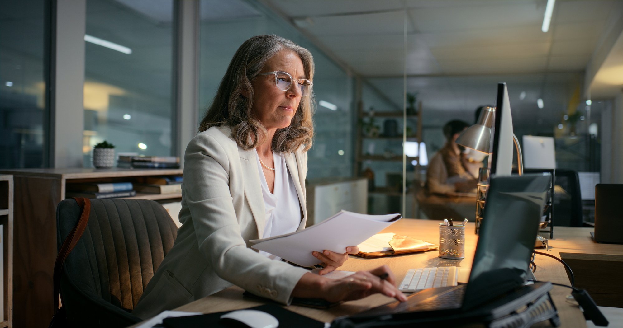 Woman working on laptop at office with dimmed lights, later in the day